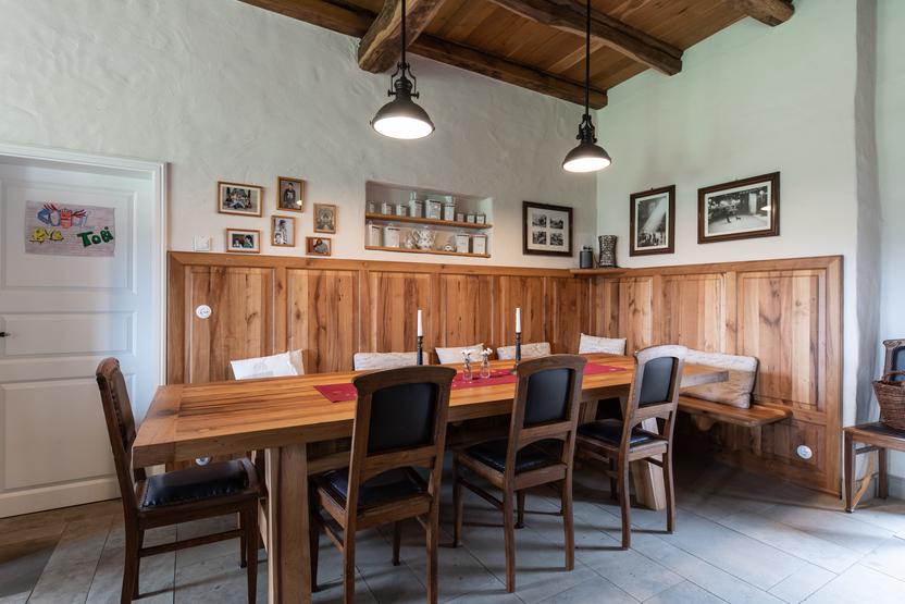 Gemütlicher Essbereich mit rustikalen Holzmöbeln Rustikaler Essbereich mit Holztisch, Stühlen, Eckbank und dekorativen Elementen wie Fotos, Kerzen und Wandregalen in einem hellen Raum mit Holzbalkendecke.