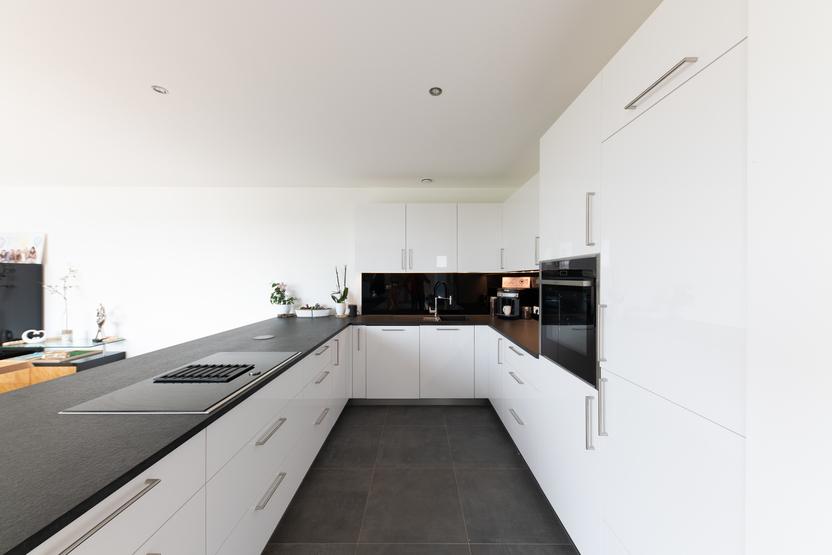 Helle, maßgeschneiderte Küche mit großem Essbereich, weißer Einrichtung und dunkler Arbeitsplatte, natürlich beleuchtet.