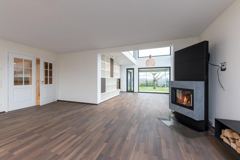 Moderner Wohnbereich mit Kamin und Gartenblick Offener Wohnbereich mit dunklem Parkettboden, Kamin, großen Fenstern mit Blick in den Garten, integrierter Regalwand und modernen Doppeltüren.