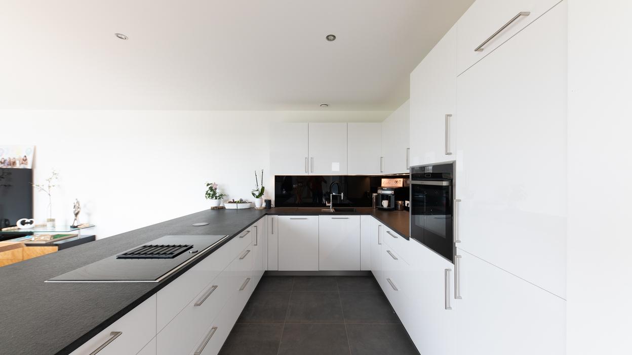 Offene Küche nach Maß im modernen Design Helle, maßgeschneiderte Küche mit großem Essbereich, weißer Einrichtung und dunkler Arbeitsplatte, natürlich beleuchtet.