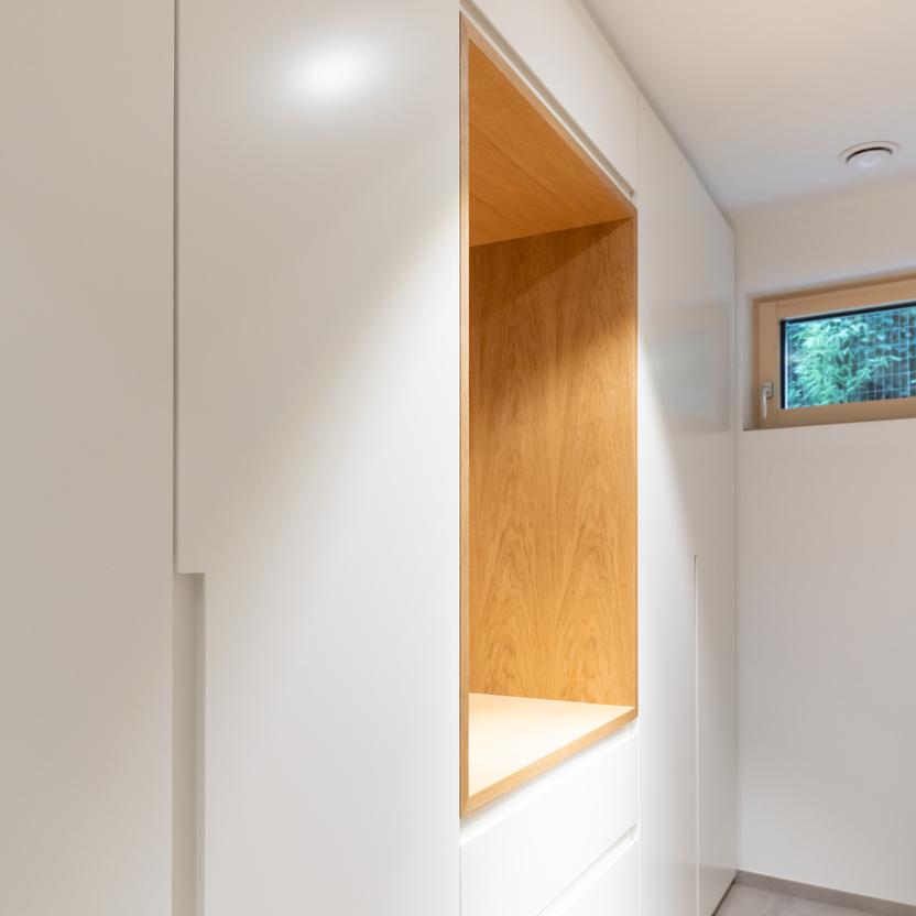 Wei&szlig;er Einbauschrank mit integriertem Holzfach in einem hellen Raum mit Fliesenboden und kleinem Fenster.
