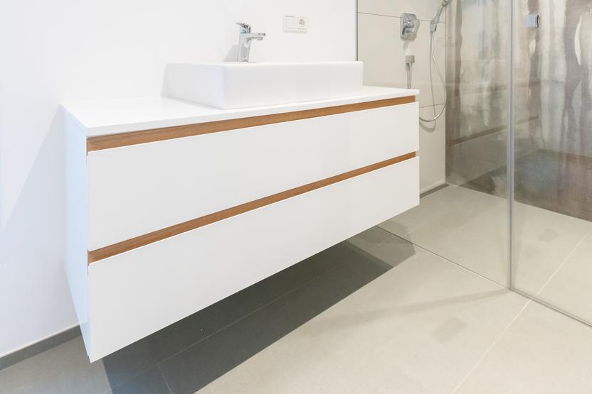 Helles Badezimmer mit rundem Spiegel und einem weißen, maßgefertigten Waschtisch mit hölzernen Details.