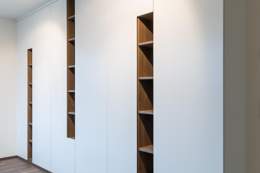 Einbauschrank mit offenen Regalelementen Moderner weißer Einbauschrank mit integrierten offenen Regalelementen aus Holz, dunklem Parkettboden und schlichter Deckenbeleuchtung.