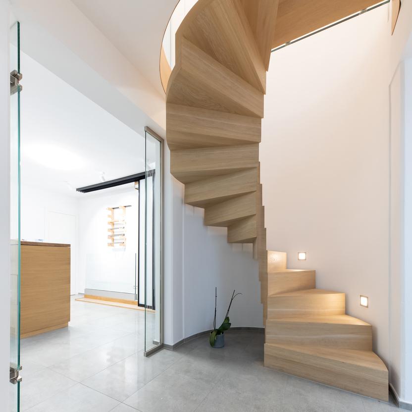Eine elegante, maßangefertigte hölzerne Wendeltreppe mit eingebauten Leuchten in einem offenen, lichtdurchfluteten Raum.