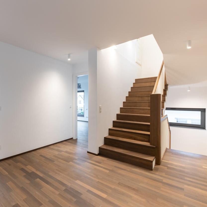 Offener Flur mit Treppe und Parkettboden Moderner Flur mit dunklem Parkettboden, Holztreppe, offenen Türen zu angrenzenden Räumen und Fenstern, die natürliches Licht hereinlassen.