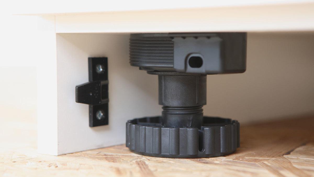 Detailaufnahme eines verstellbaren schwarzen Bodensockels mit Schraubmechanismus